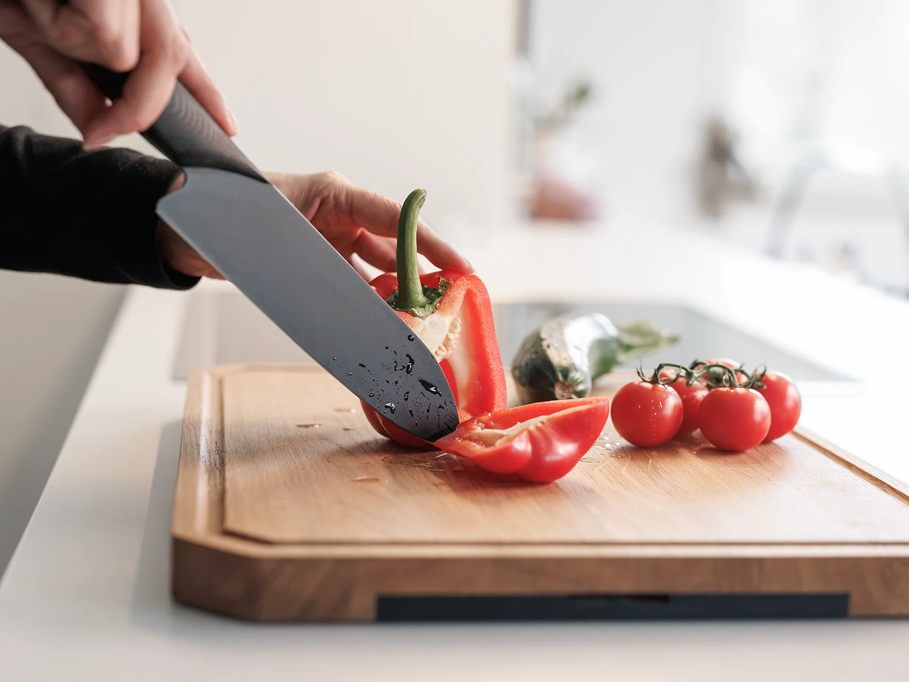 Person schneidet eine rote Paprika mit dem Darkline Fly Wheel Cut L Messer von TYROLIT LIFE auf dem WOLFBOARD.life Eichenbrett auf einer weißen Küchenzeile